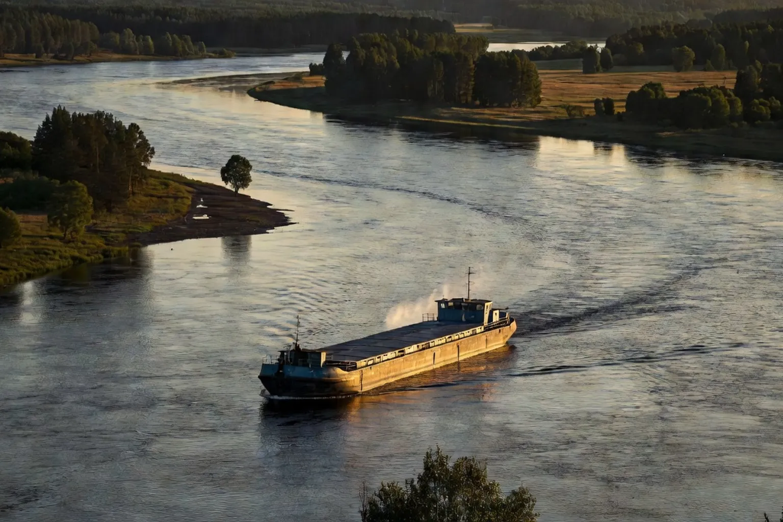 Grand fleuve russe large et puissant aux berges boisées, barge de fret à la lumière du soir