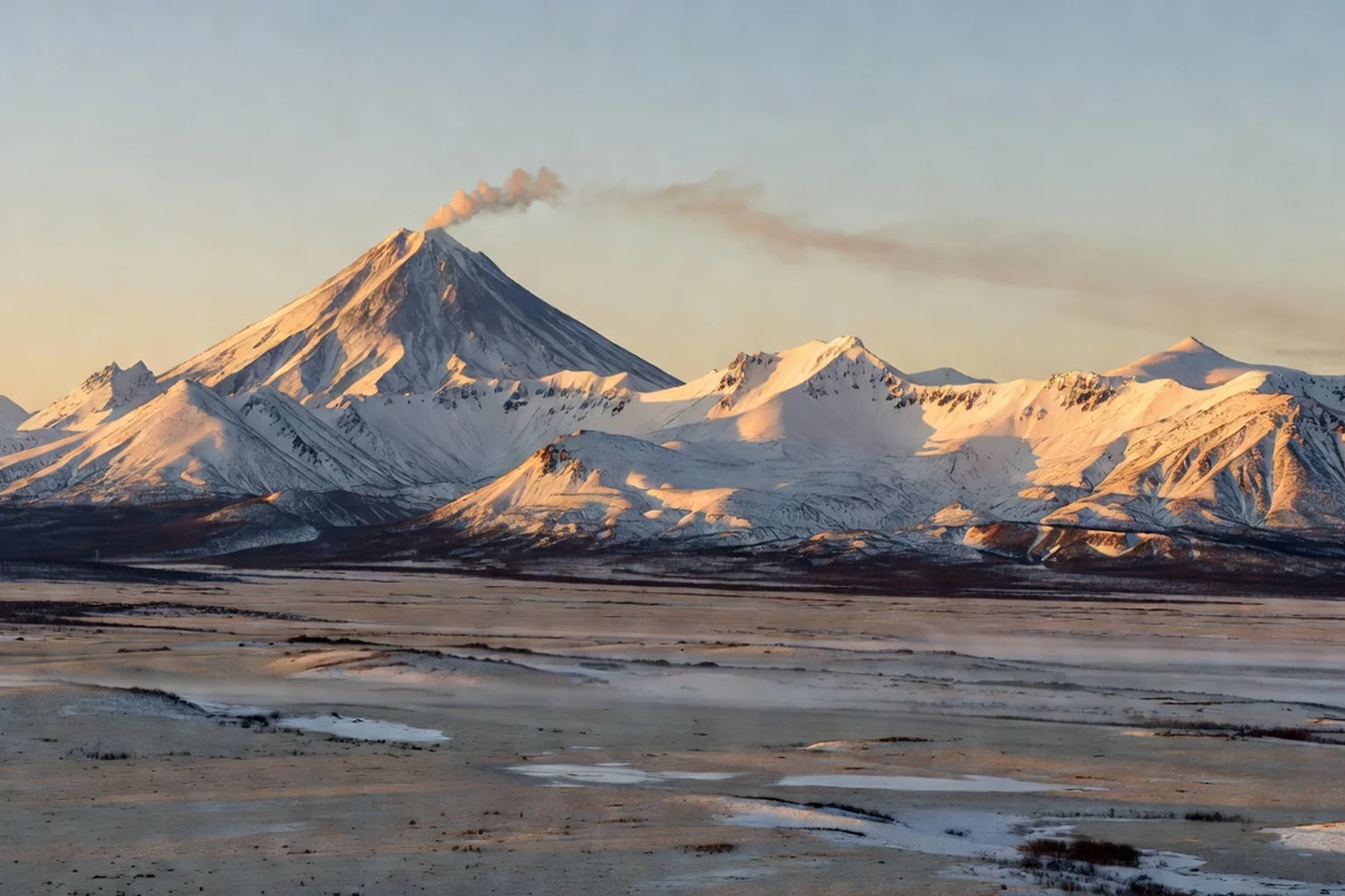 Le volcan Klioutchevskoï fumant au-dessus de la toundra de la péninsule du Kamtchatka au lever du jour